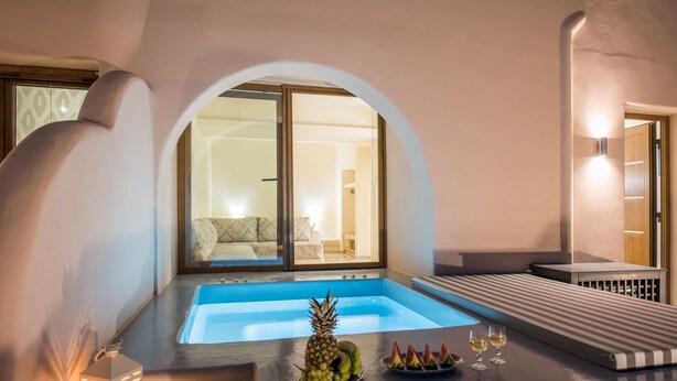Una habitació d'hotel moderna amb piscina privada, zona de menjador amb fruita i gots de vi, i vista de l'interior a través d'una porta de vidre.