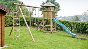 Een houten speelconstructie met een glijbaan en klimelementen in een gazon.