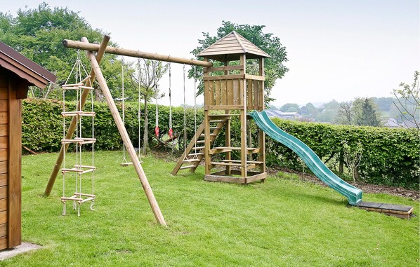Una estructura de juego de madera con un tobogán y elementos para escalar en un patio cubierto de césped.