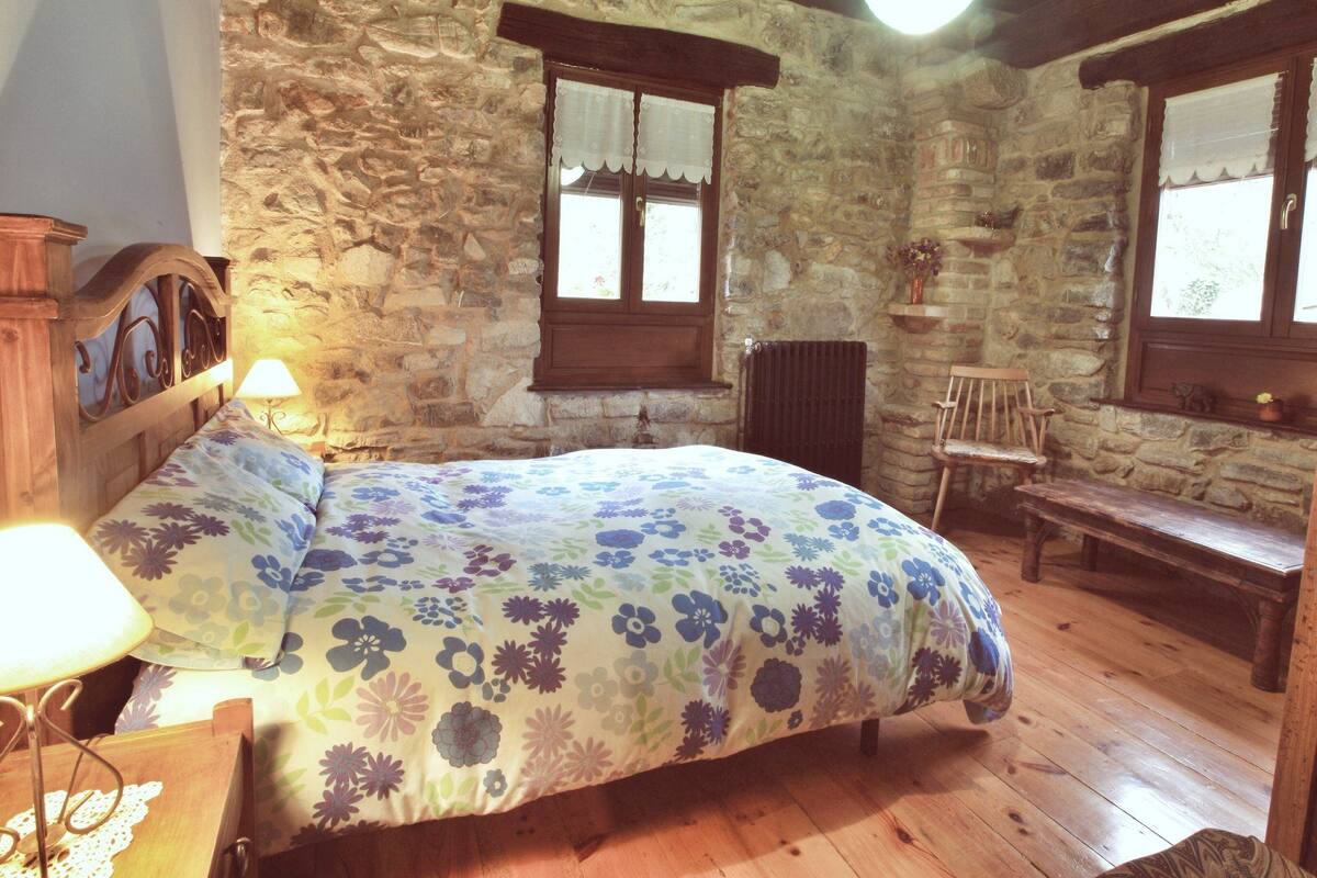 A rustic bedroom with a stone wall, wooden bed, and a bench.