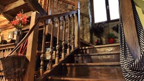 Un escalier en bois, avec un mur en pierre et une fenêtre, qui mène à l’étage supérieur.