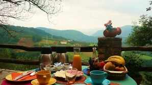 Une table mise pour le petit-déjeuner, avec en arrière-plan une vue panoramique sur des collines.
