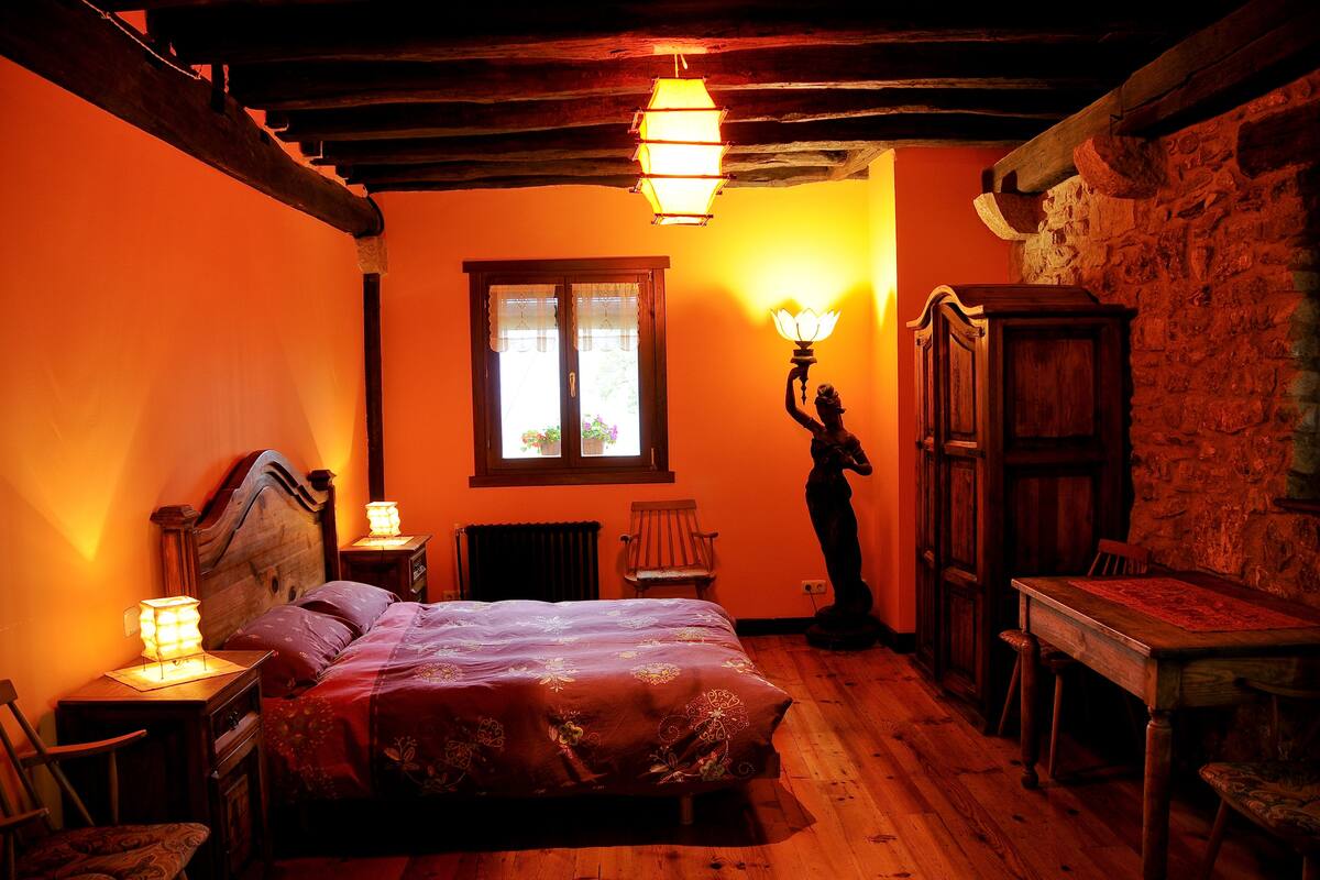 A cozy bedroom with a wooden bed, a nightstand, a chair, a table, and a statue.