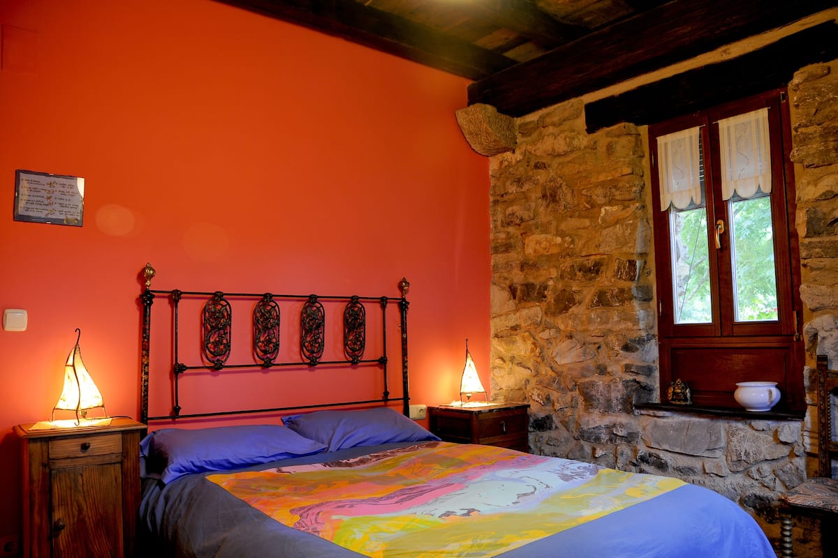 A bedroom with a stone wall, a wooden bed frame, and a window with curtains.