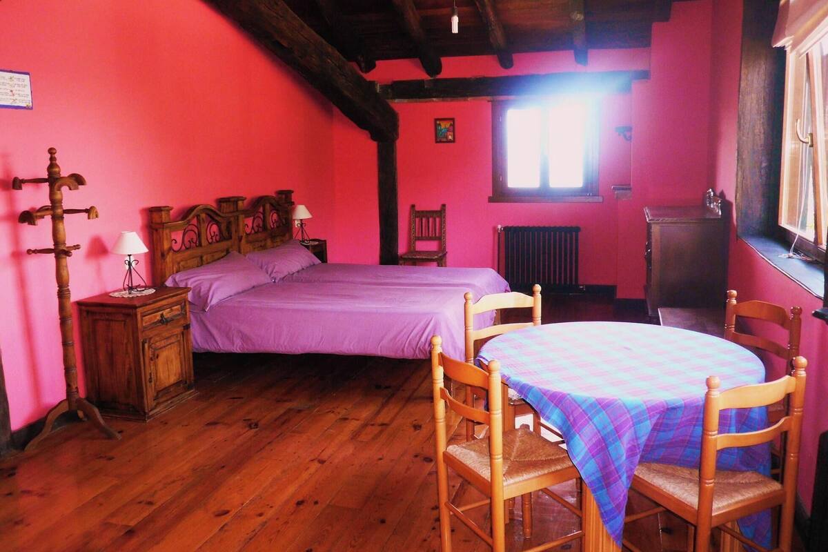 A bedroom with a wooden bed, a nightstand, a chair, and a table with a plaid tablecloth.