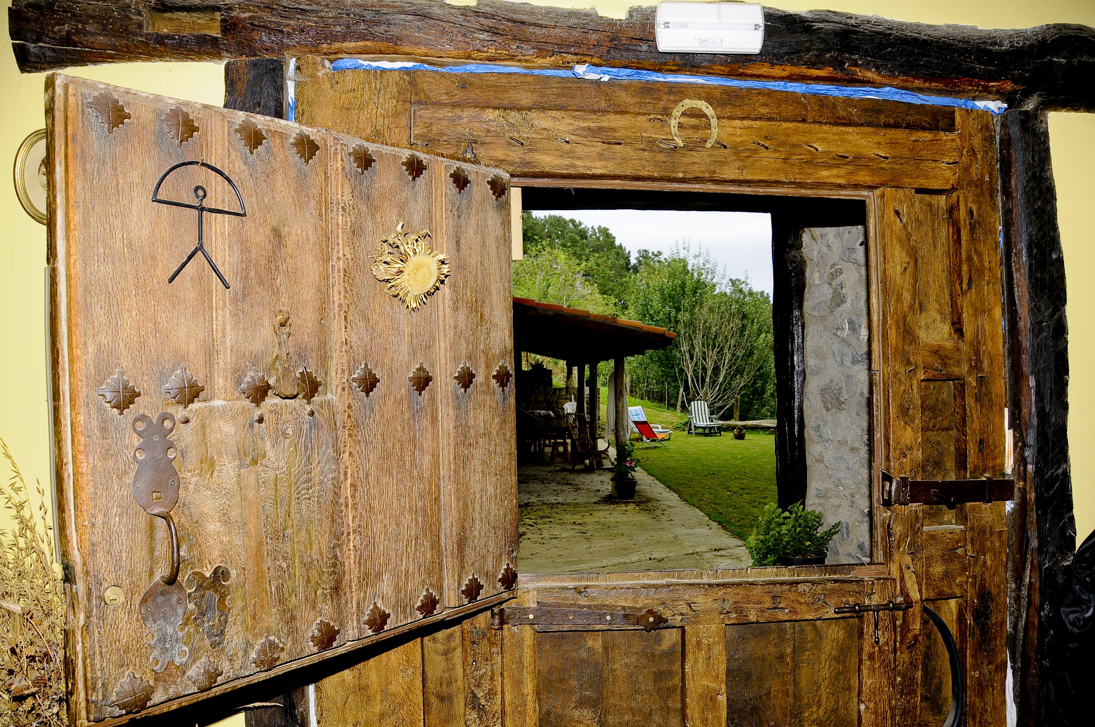 A rustic wooden door with a metal handle and decorative elements, leading to an outdoor area with a covered seating area and a lawn.