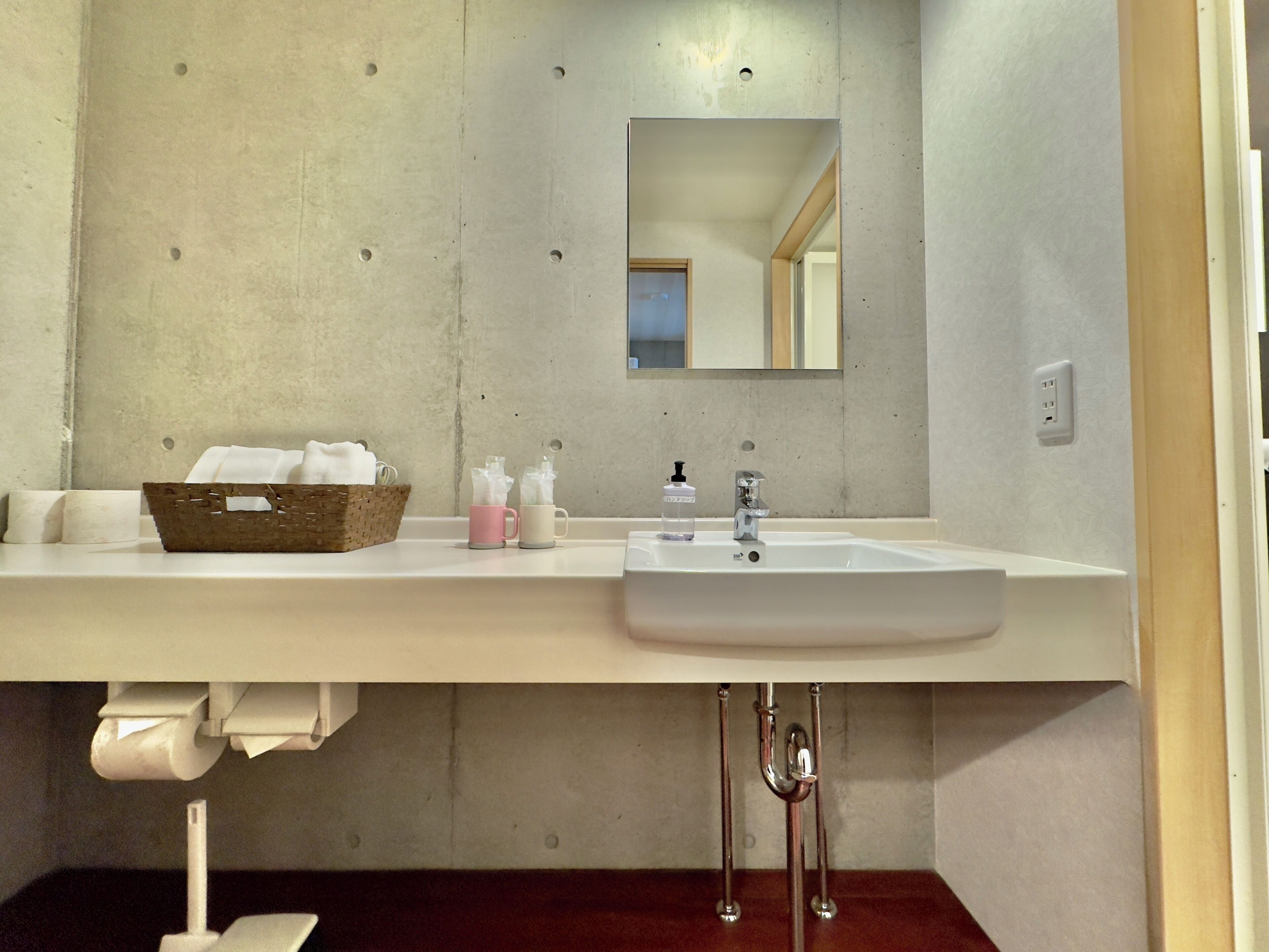 A bathroom with a white sink, a mirror, a wooden basket, and a towel rack.