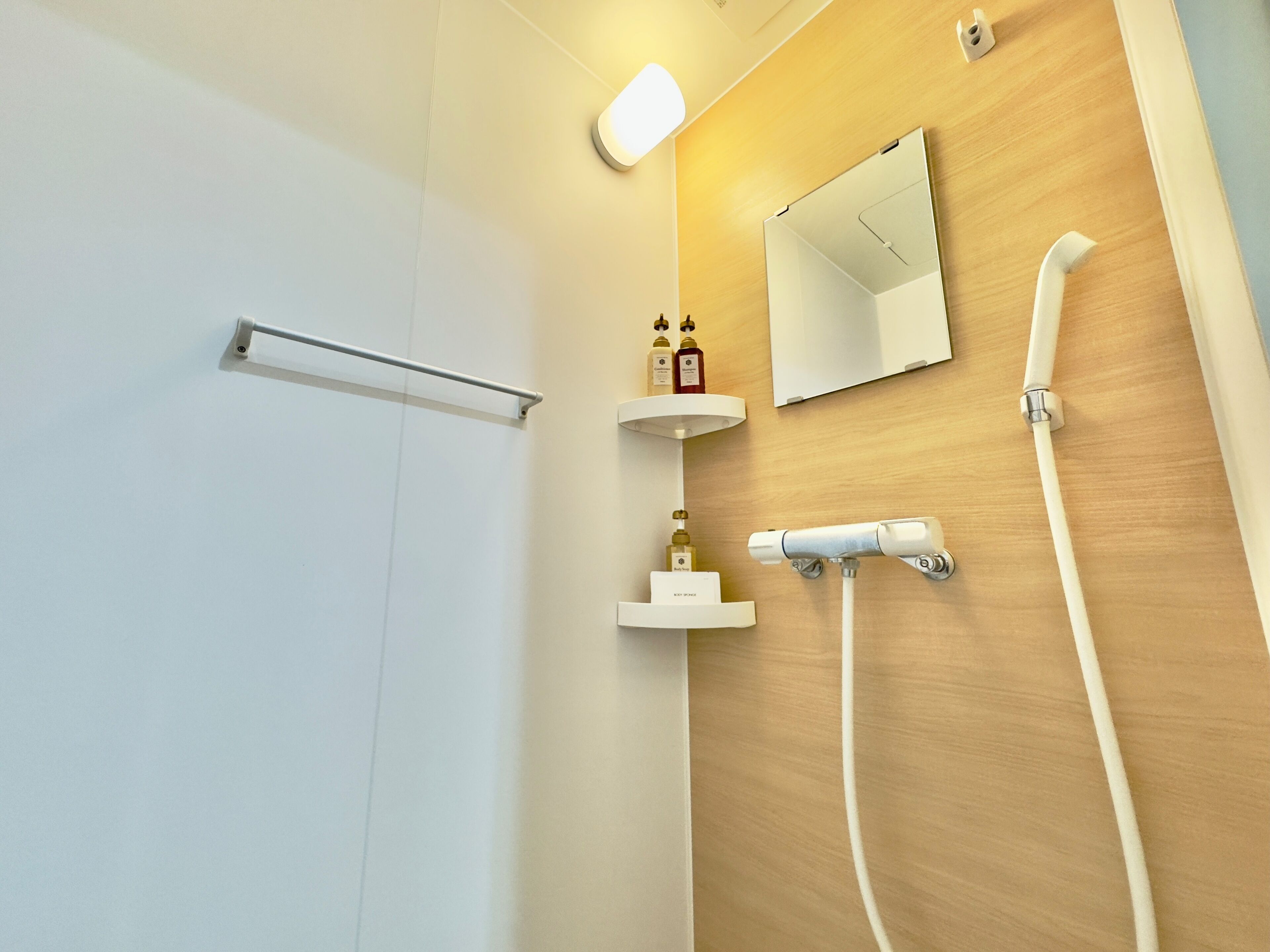 A modern bathroom with a wooden vanity, a mirror, a towel rack, and a shower with a handheld showerhead.