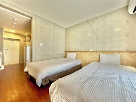 A hotel room with two beds, a wooden headboard, a concrete accent wall, and a door leading to a bathroom.