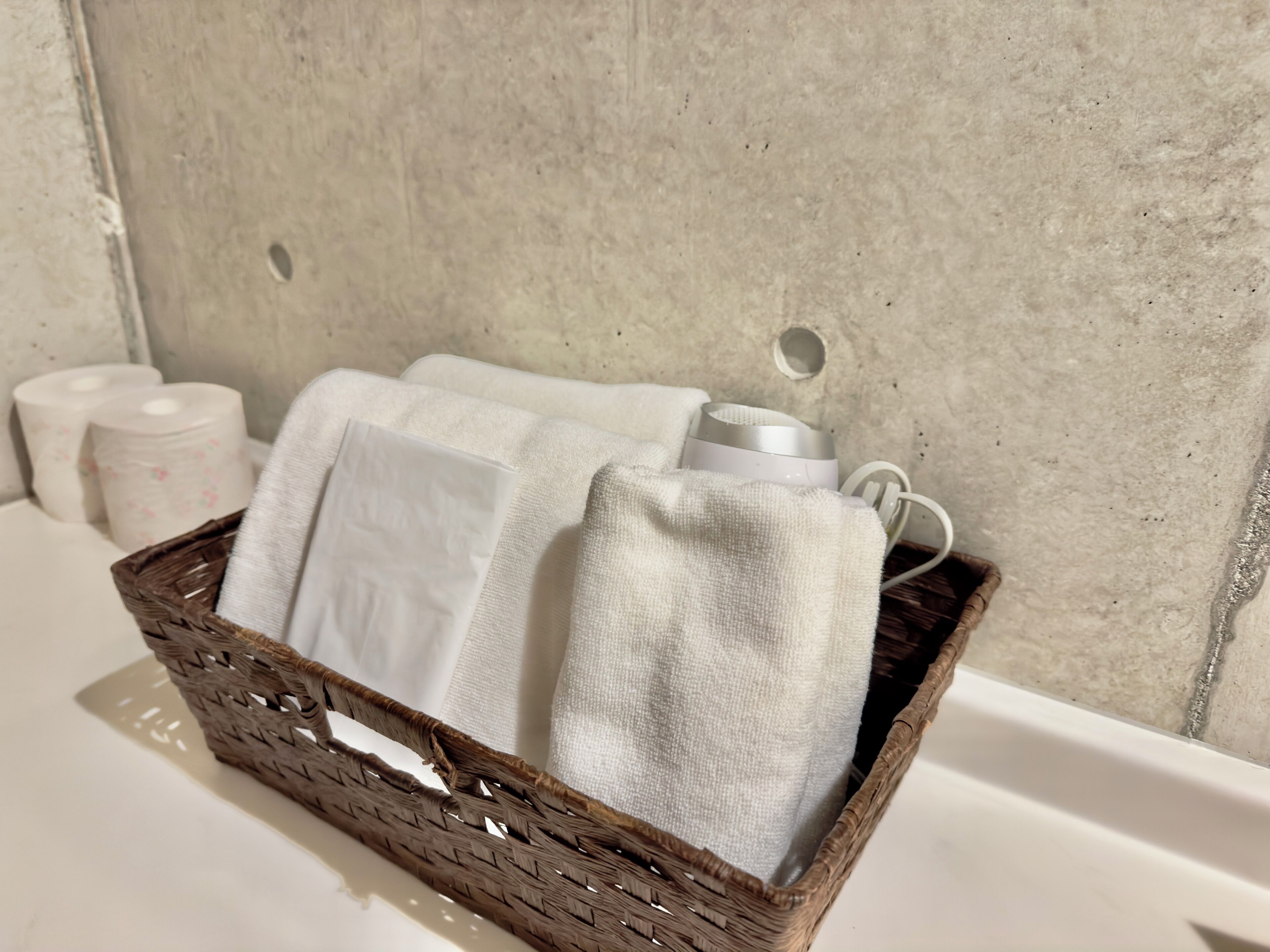 Un baño con una cesta de madera que contiene toallas blancas y una botella blanca.