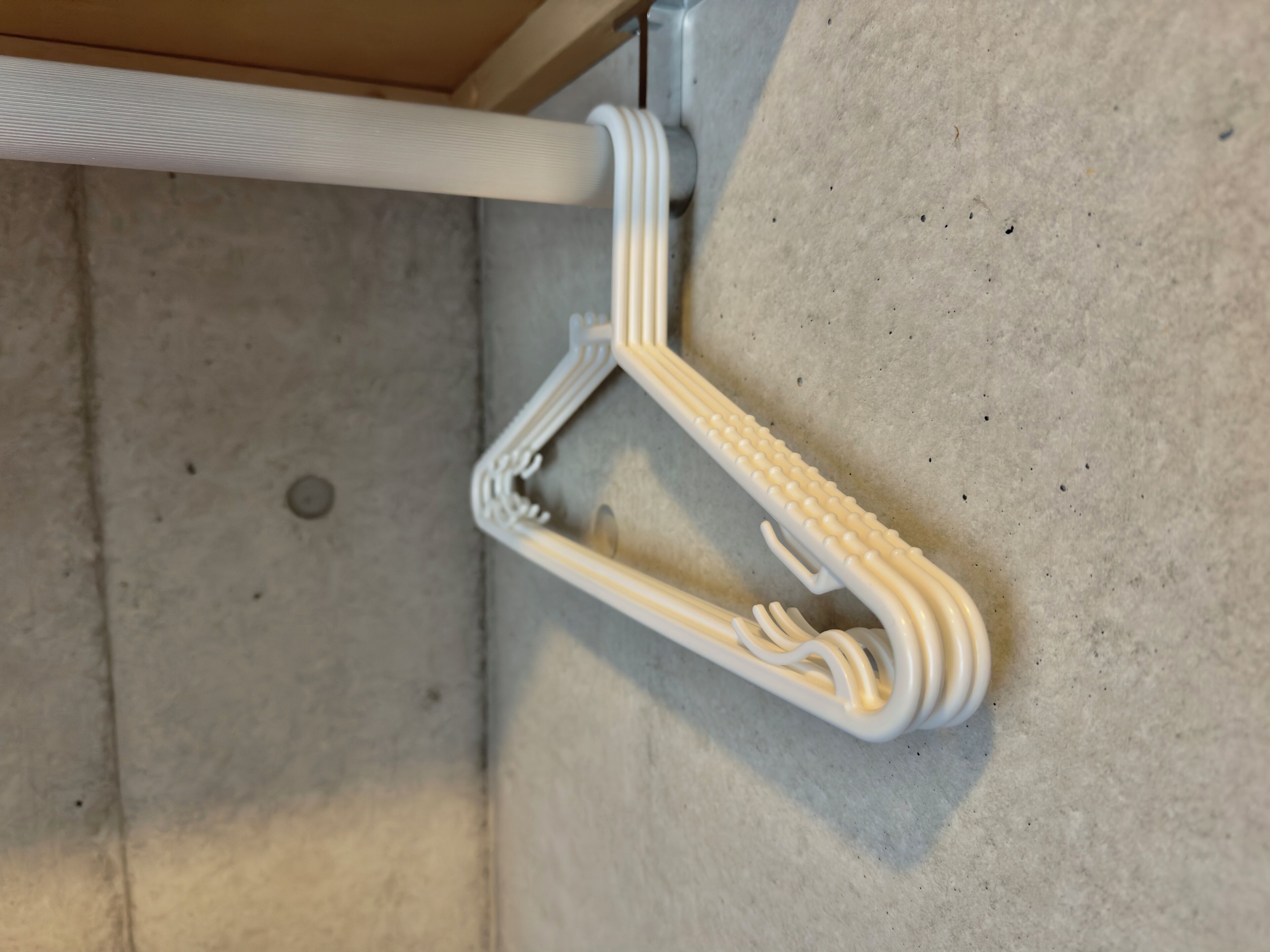 A white, uniquely shaped hanger with a curved design, attached to a white pipe on a concrete floor.