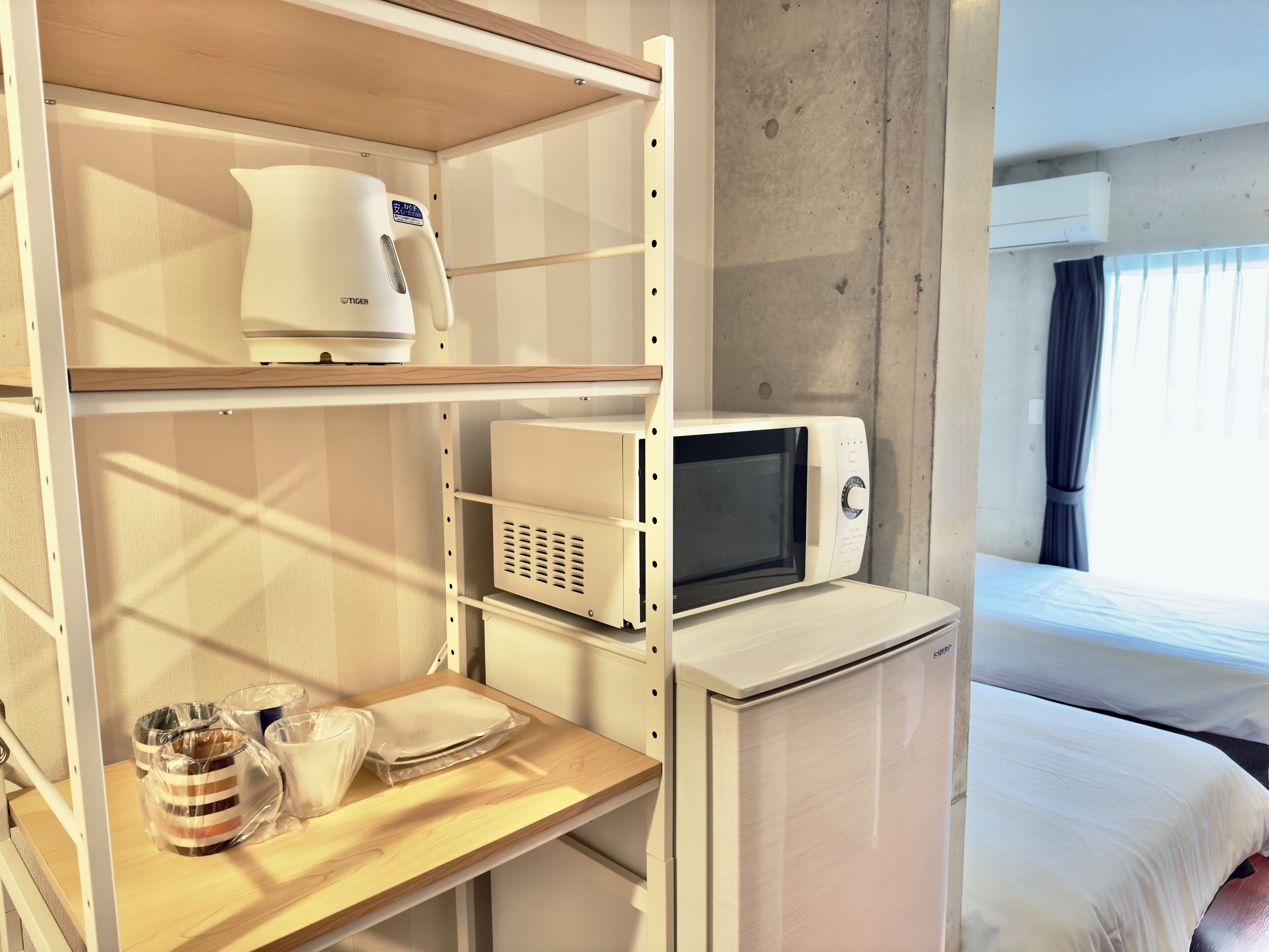 Habitación de hotel con cama, microondas, cafetera y una mesita con una taza y un frasco.