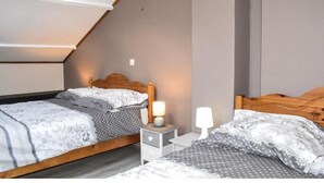 A bedroom with two beds, wooden headboards, bedside tables with lamps, and a sloped ceiling.