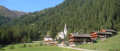 A rural village with traditional wooden houses, a church, and a mountain backdrop.
