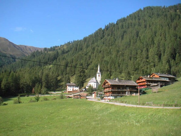 A rural village with traditional wooden houses, a church, and a mountain backdrop.