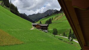 Una cabaña de montaña con fachada de madera, rodeada de colinas verdes exuberantes y un cielo despejado.
