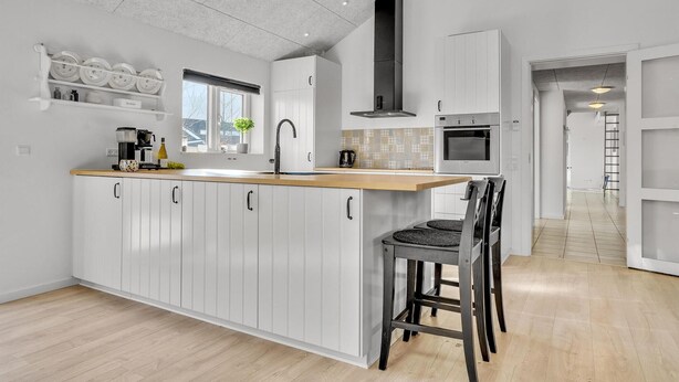 A modern kitchen with white cabinetry, a wooden countertop, a built-in stove, and a black range hood. - Pet friendly home in Hadsund with sauna (Hadsund)
