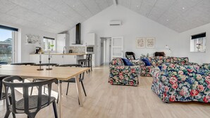 A spacious living area with a high ceiling, a dining area with a wooden table and chairs, and a kitchen with white cabinets and a black range hood. - Pet friendly home in Hadsund with sauna (Hadsund)
