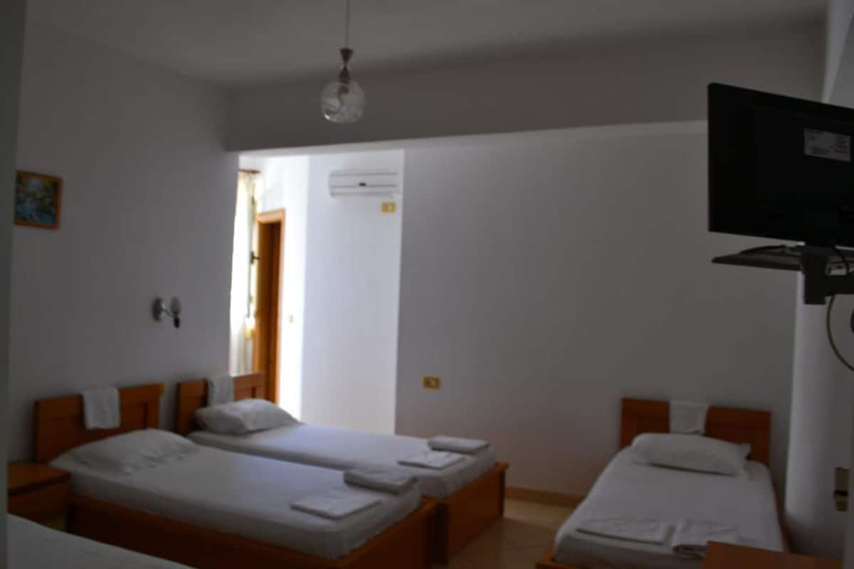 A hotel room with two single beds, a television mounted on the wall, and a door leading to another room.