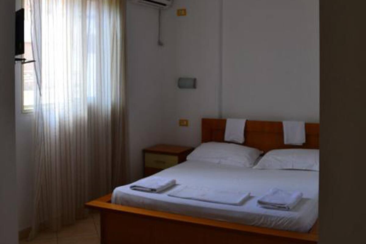 A single bed with white linens, a wooden headboard, and a nightstand with a lamp.