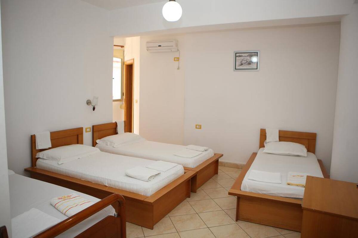 A room with four single beds, a wooden bench, a small table, and a wall-mounted air conditioner.