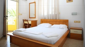A hotel room with a bed, a desk, a chair, a bedside table, and a window with curtains. - Hotel Alpine (Vlorë)
