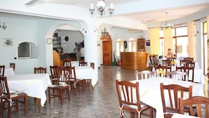 A dining area with multiple tables and chairs, a ceiling fan, and a chandelier. - Hotel Alpine (Vlorë)