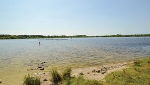 Un lac paisible, avec une jetée qui s’avance sur l’eau, bordé de rives verdoyantes et d’une côte boisée.