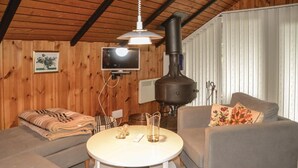 Une pièce chaleureuse avec des murs en bois, un canapé, une table ronde avec un plateau en verre et une cheminée.