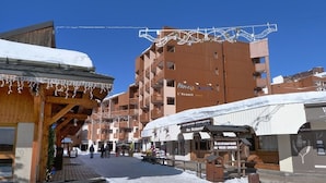 A snowy outdoor area with wooden buildings, a restaurant sign, and a ski lift in the background.