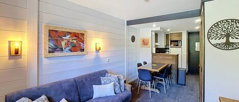 A modern living room with a sofa, a dining table with chairs, and a kitchen in the background.