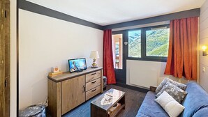 A living room with a sofa, a wooden cabinet, a television, and a window with curtains.