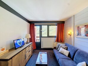 A furnished room with a sofa, a coffee table, a TV on a wooden cabinet, and a window with curtains.