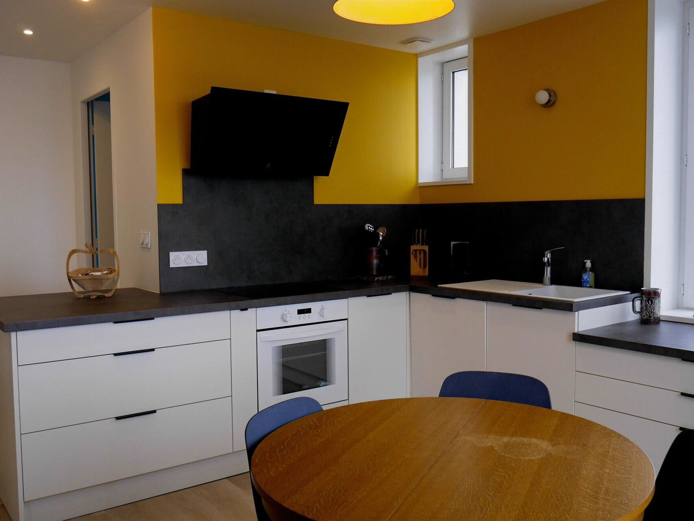 A modern kitchen with white cabinets, a black countertop, and a wooden dining table.