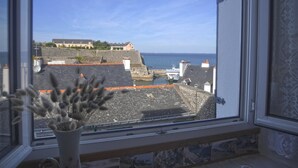 A view through a window of a coastal town with buildings, a sea wall, and a large building on a hill. - Central apartment with sea view terrace, pets allowed (Le Palais)