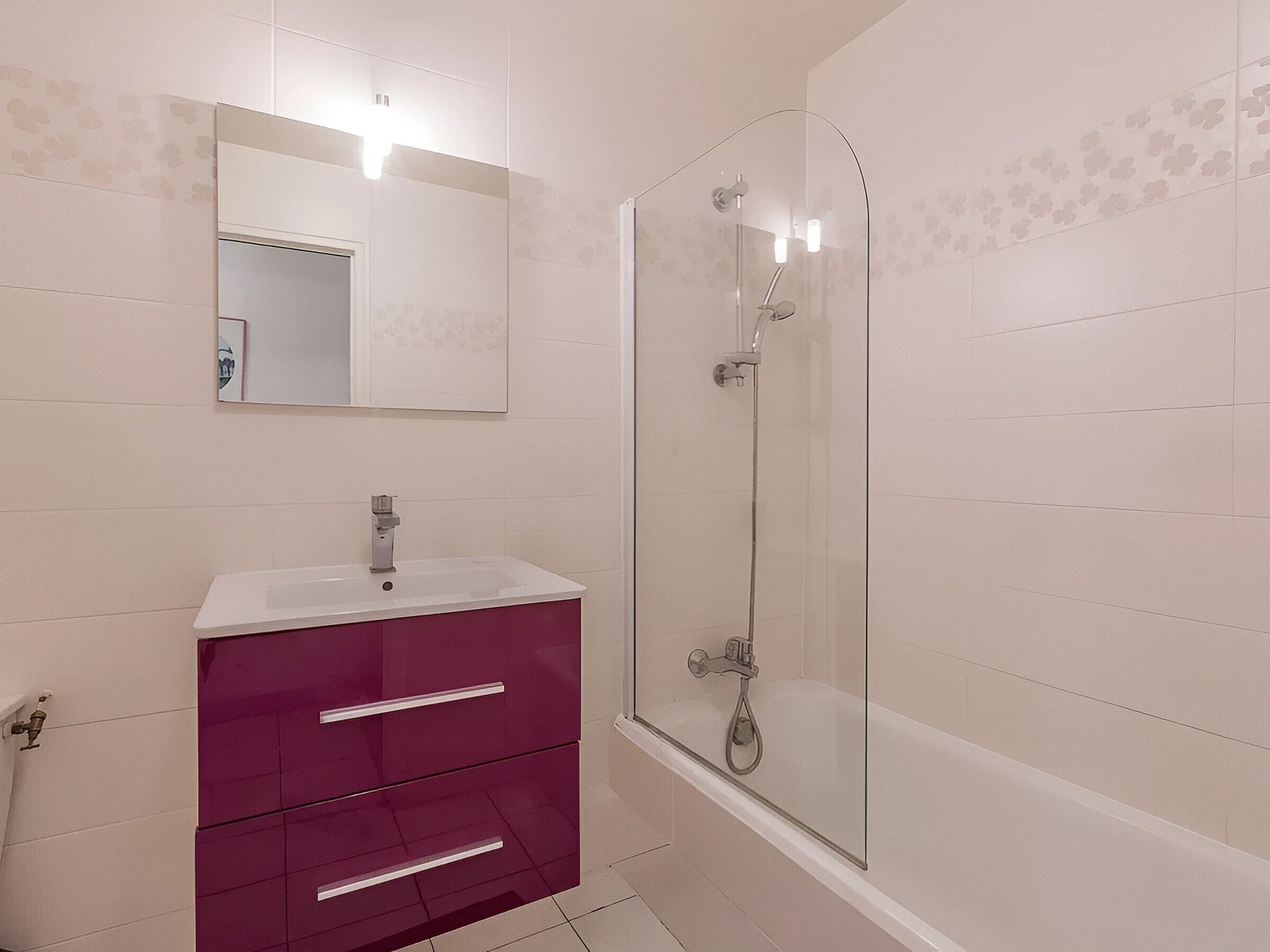 Een badkamer met een witte wastafel, een spiegel, een douche met glazen wanden en een paars badkamermeubel.