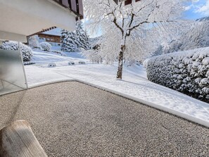 A snow-covered outdoor area with a pebble path, a wooden bench, and snow-laden trees.