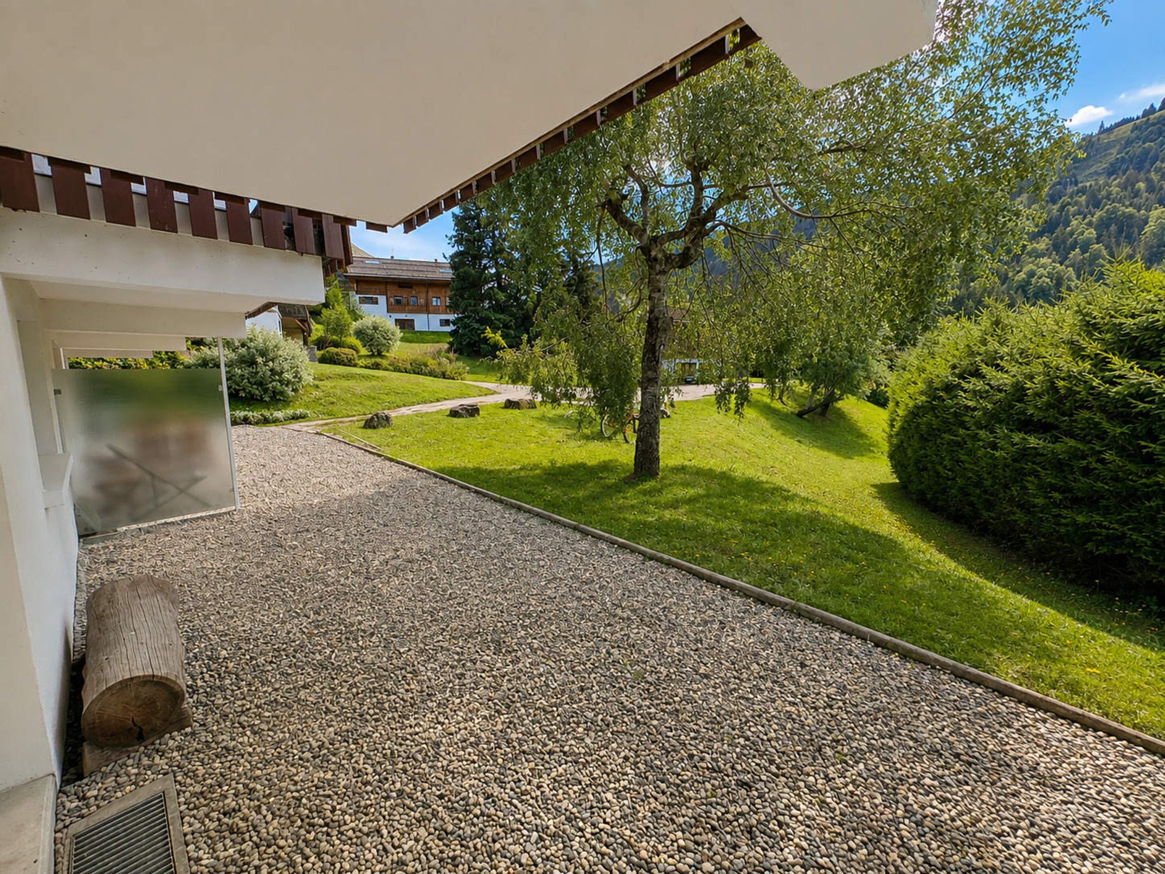 Un camí que condueix a un edifici amb rebedor cobert, envoltat d'un jardí ben cuidat i vistes a una vessant de muntanya.