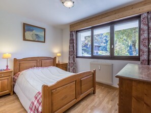 Un dormitorio con una cama de madera, dos mesitas de noche con lámparas, un radiador y una ventana con cortinas.