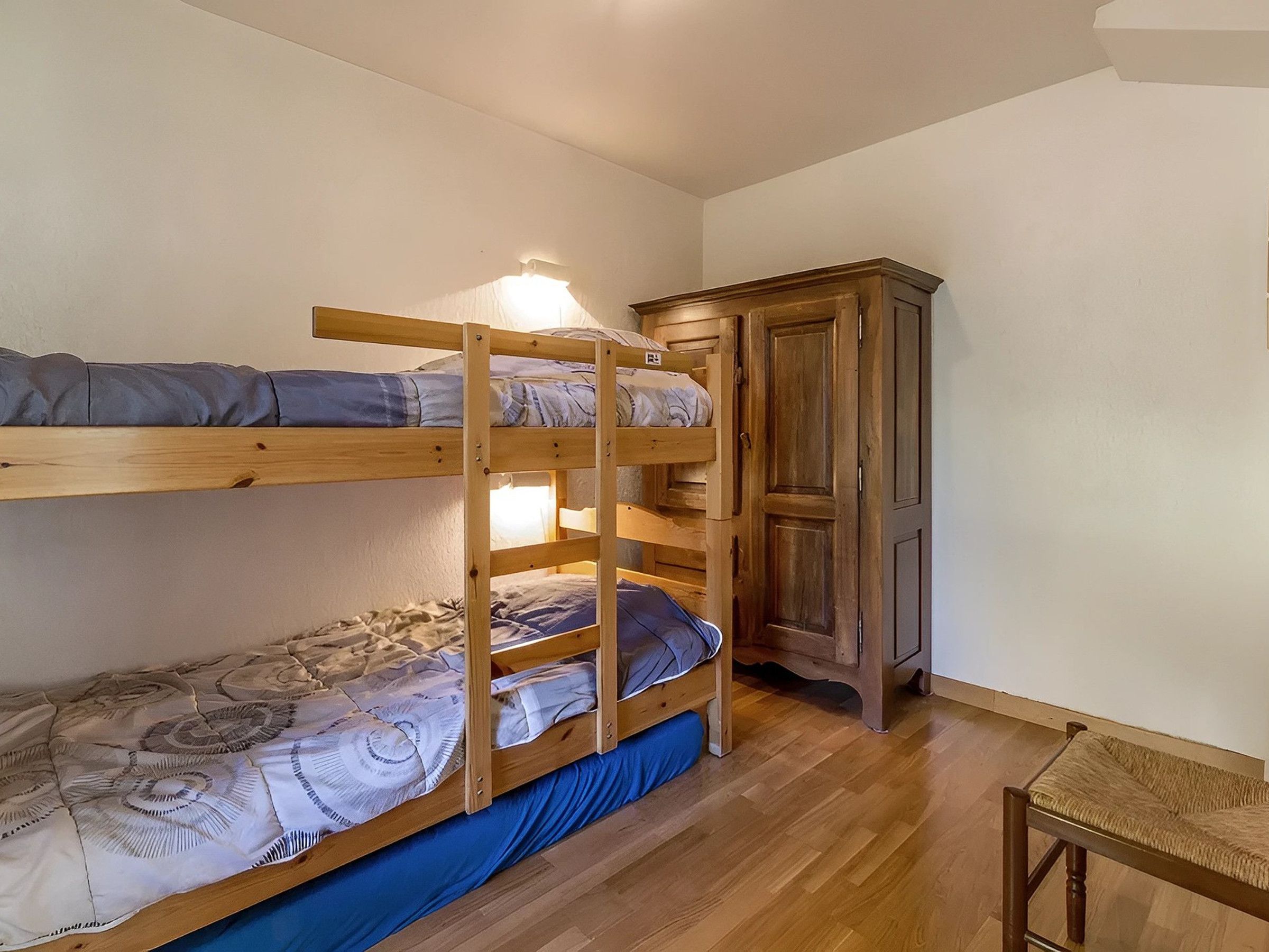 A bunk bed with a wooden cabinet and a chair in a room with wooden flooring.