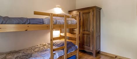 Un lit superposé avec une armoire en bois et une chaise dans une pièce dont le sol est recouvert de planches de bois.