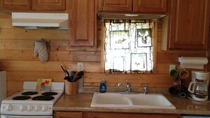 Una cocina con armarios de madera, una estufa, un fregadero y una ventana con vistas a la vegetación.