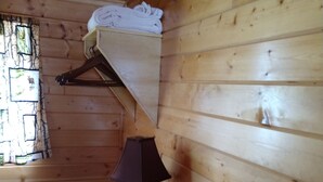 Interior de una cabaña de madera con un perchero, una mesa con una lámpara, una cesta y una caja de pañuelos.