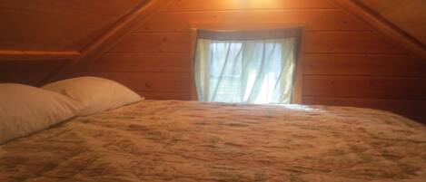 A bedroom with a wooden ceiling, a bed with a floral bedspread, and a window with curtains.