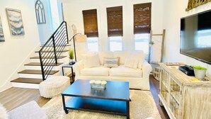 Un salon moderne avec un escalier, un canapé blanc, une table basse et un téléviseur posé sur un meuble en bois.