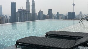 En infinitypool med solstolar, omgiven av en stadsbild med höga skyskrapor.