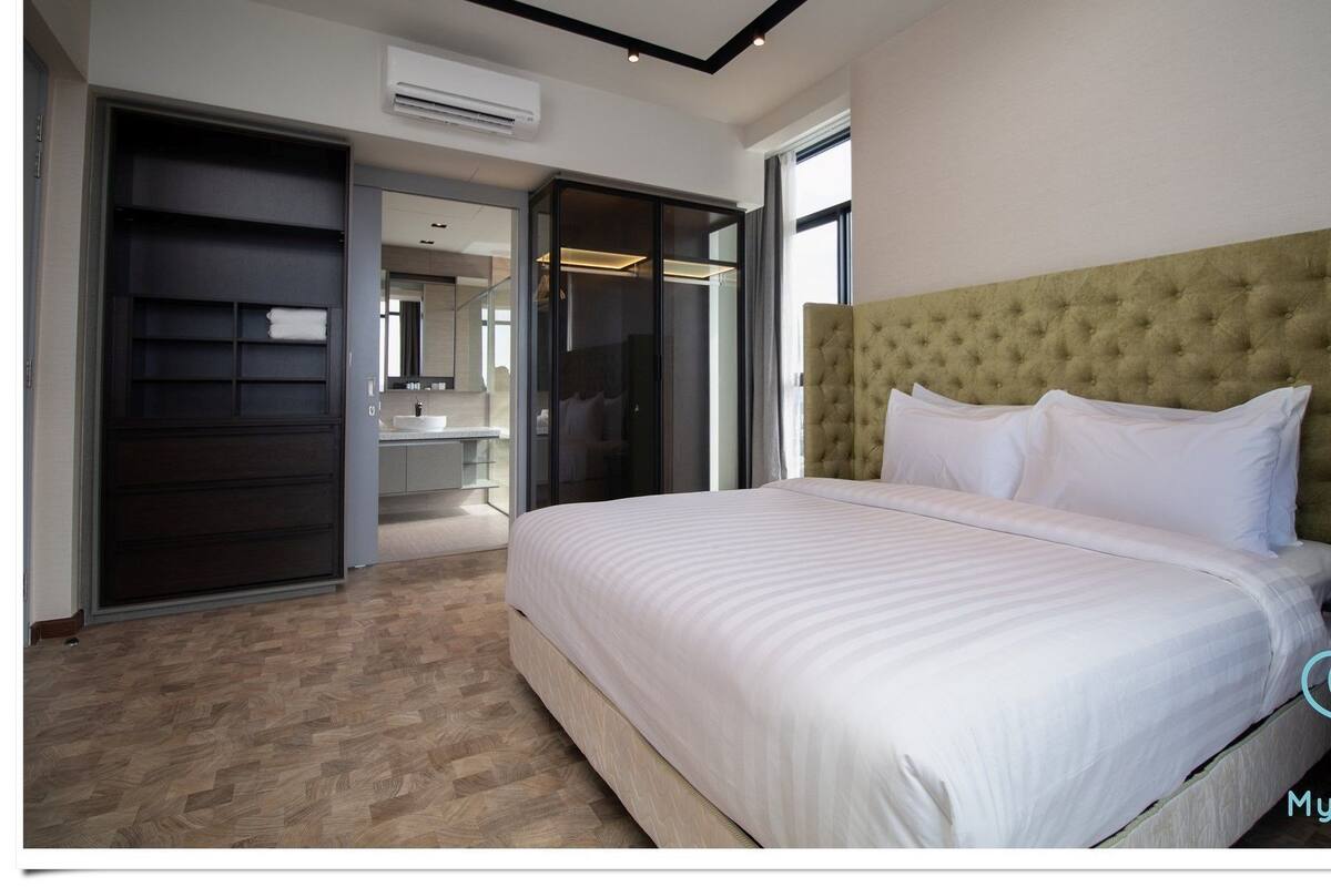 A modern hotel room with a large bed, a walk-in closet, a bathroom with a mirror, and a ceiling with recessed lighting.