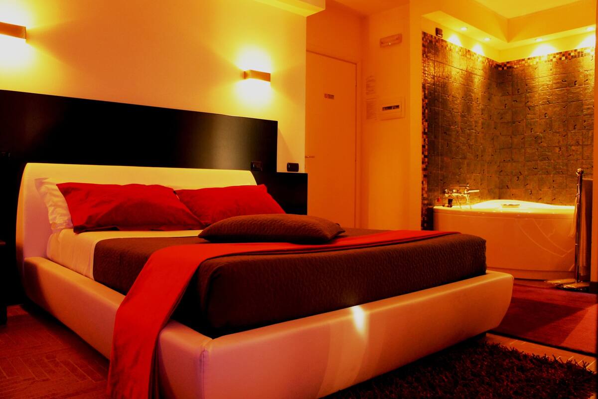 A modern hotel room with a large bed, a separate bathroom with a bathtub, and a red carpet.