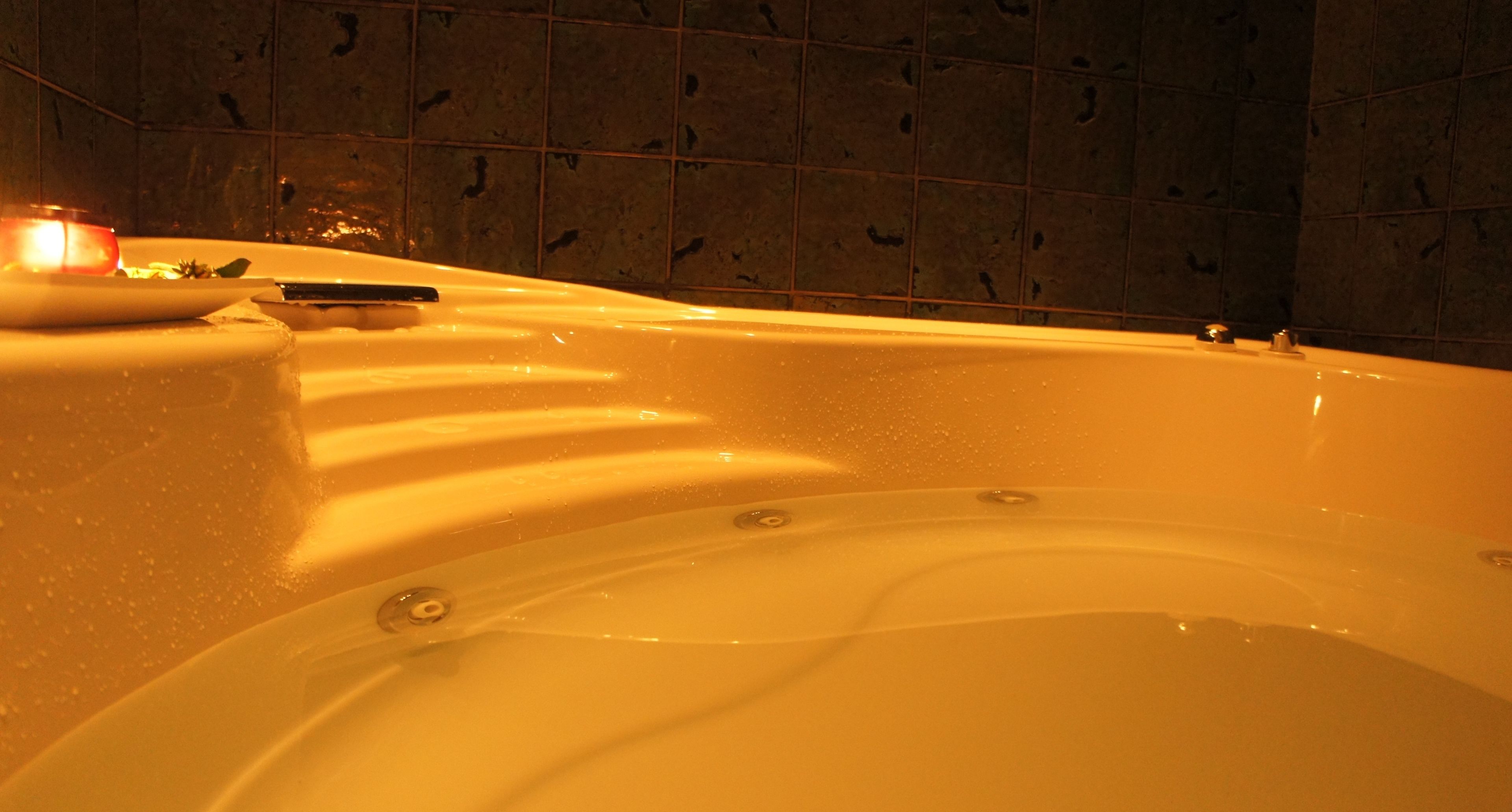 Eine Badewanne mit Kerze und Buch, umgeben von gefliesten Wänden.