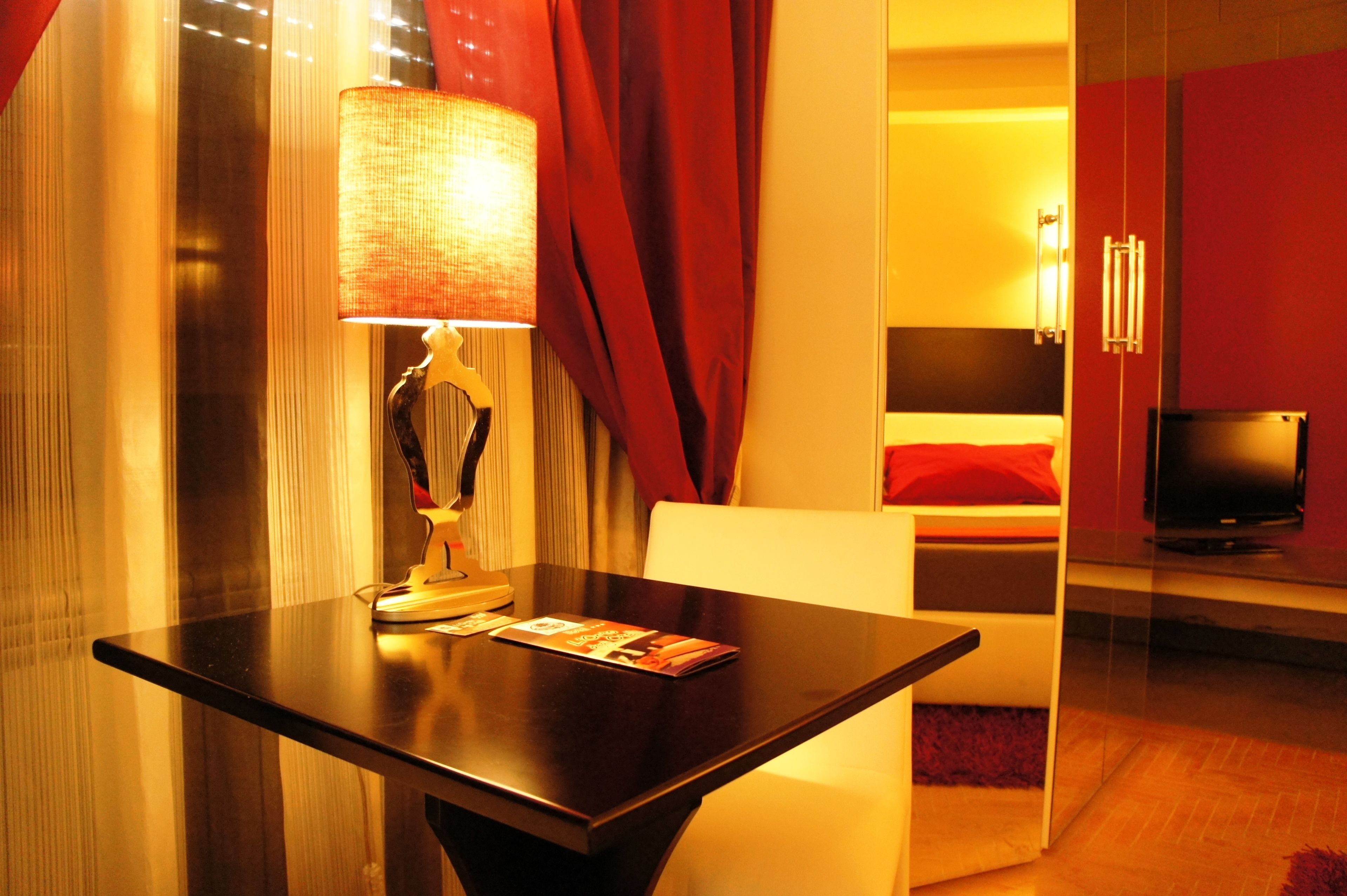 A hotel room with a bed, a TV, a table with a lamp, and red curtains.